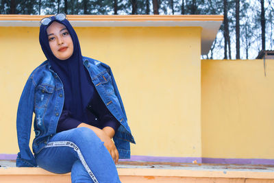 Portrait of woman sitting against blue wall