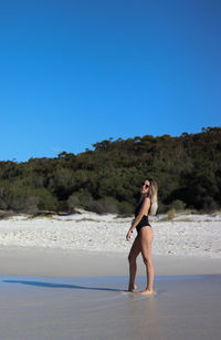 Side portrait of young woman in black bikini and brown sunglasses on beach in eastern australia