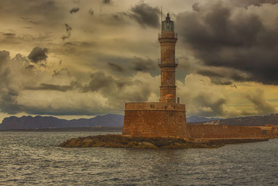 Lighthouse on building by sea against cloudy sky