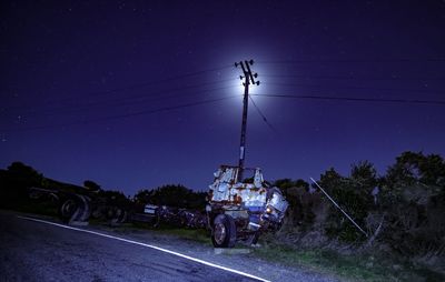 Cars on road amidst illuminated field against sky at night