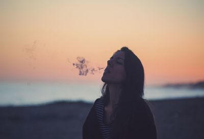 Portrait of young woman standing on beach during sunset