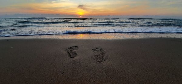 Footprints on sand at beach against sky during sunset