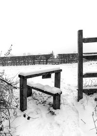 Bench on snow covered field against clear sky