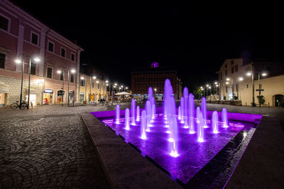 Illuminated fountain by building in city at night