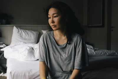 Thoughtful lonely woman looking away sitting in bedroom at home