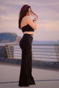 Woman standing by railing against sea during sunset