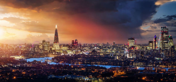 Illuminated buildings in city against cloudy sky