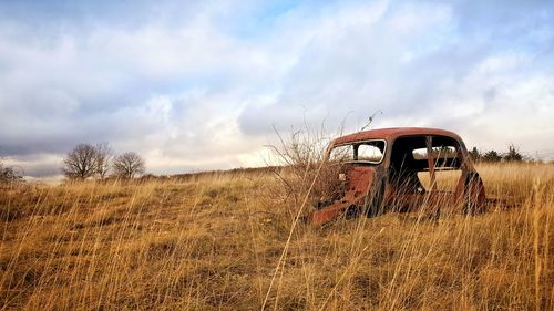 Abandoned car on field against sky