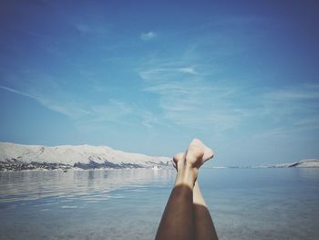 Low section of person by sea against sky