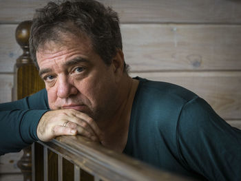 Portrait of mature man leaning on wooden railing at home