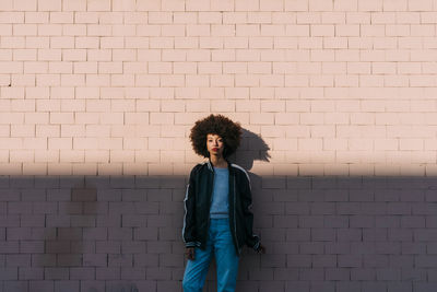 Woman staring while leaning on brick wall