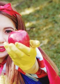 Portrait of young woman wearing costume holding apple while standing outdoors