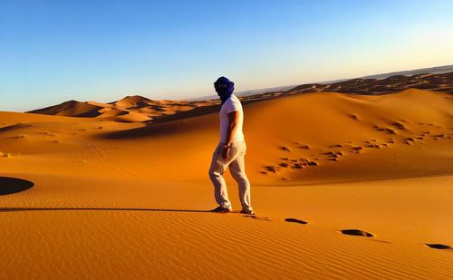 Full length of woman standing on sand dune against clear sky