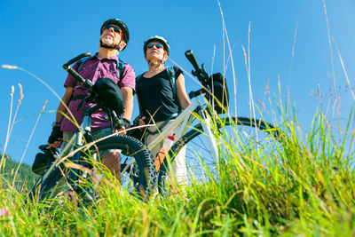 Full length of happy friends sitting on grassy field against clear sky