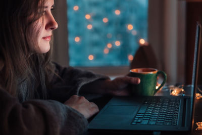 Young beautiful woman sits in front of laptop with cup of tea and looking at screen. 