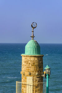 Lighthouse by sea against clear sky