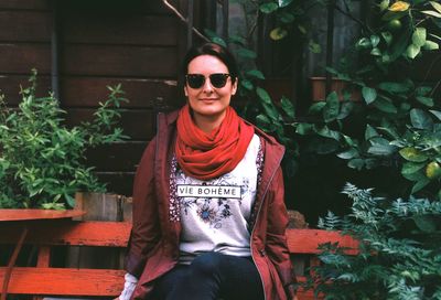 Portrait of smiling woman sitting on bench amidst plants at yard