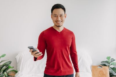 Portrait of young man using mobile phone while standing against wall