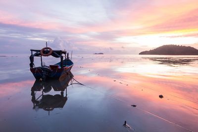 Boat moored on sea against sky during sunset