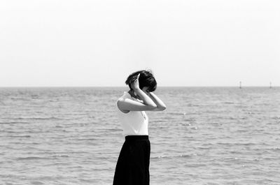 Side view of young woman standing at beach against sky during sunny day