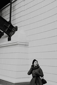 Woman in warm clothes standing outdoors against wall