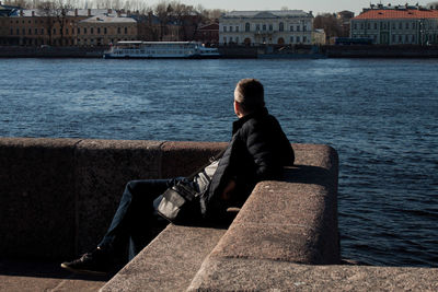 Side view of man sitting on seat against sea