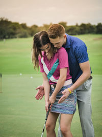 Young woman playing golf with man