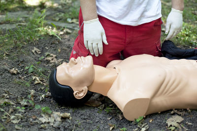 Low section of man practicing cpr on dummy at field