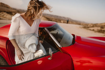 Bride and groom resting near luxury red vehicle during trip through bardenas reales natural park in morning in navarra, spain
