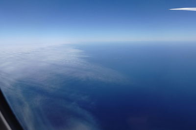 Aerial view of aircraft wing over sea against blue sky
