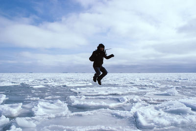 Man jumping on snow covered lake against sky