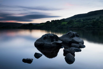 Rocks in lake against sky at dusk