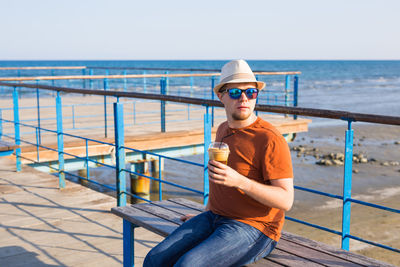 Portrait of man sitting on railing against sea