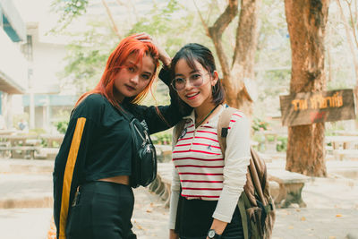 Portrait of female friends standing against trees