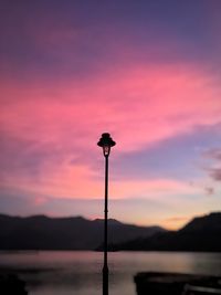 Silhouette street light by lake against romantic sky at sunset