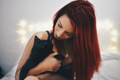 Close-up of young woman holding cat while sitting on bed at home