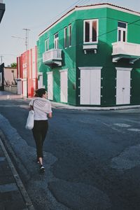 Rear view of woman walking on road by building