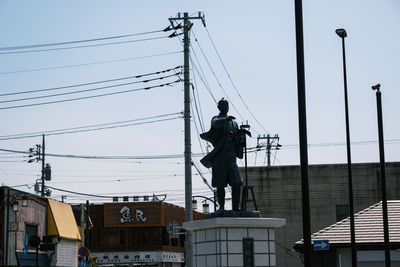 Low angle view of statue against electricity pylon