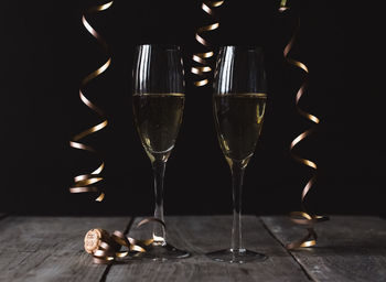 Two glasses of champagne on wooden table with black background.