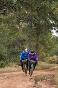 People in protective helmet and colorful jacket riding bikes in forest during bike packing adventure