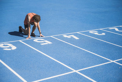 Young athlete kneeling at starting line on sunny day