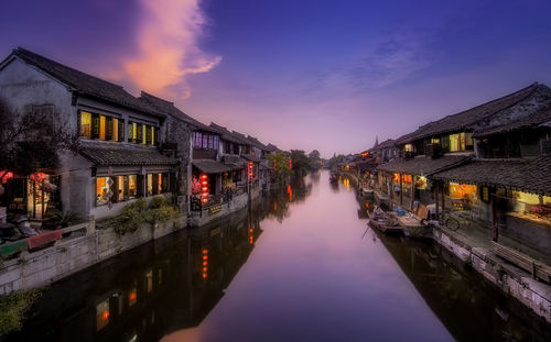 Illuminated houses by river against sky