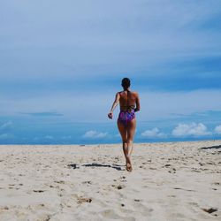Full length rear view of woman in swimwear walking at beach against sky