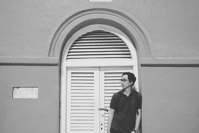 Thoughtful young man standing against closed window amidst wall