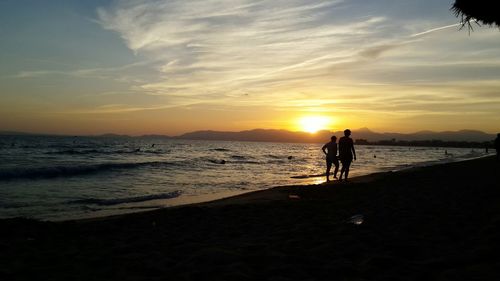 Silhouette people on beach against sky during sunset
