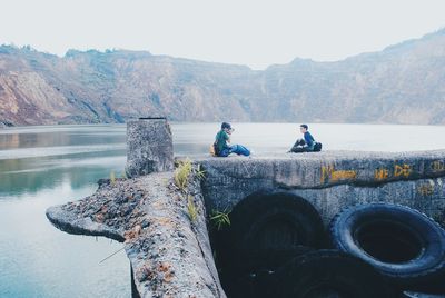 Friends sitting on retaining wall by river