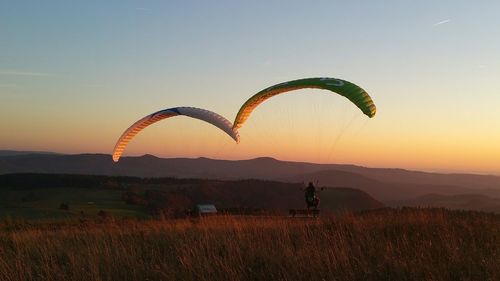 Person paragliding on field against sky during sunset