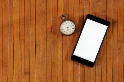 Smart phone and pocket watch on wooden table