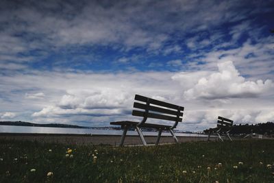 Empty bench on field against sky