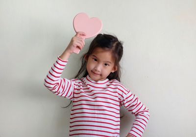 Portrait of cute girl holding heart shape against wall